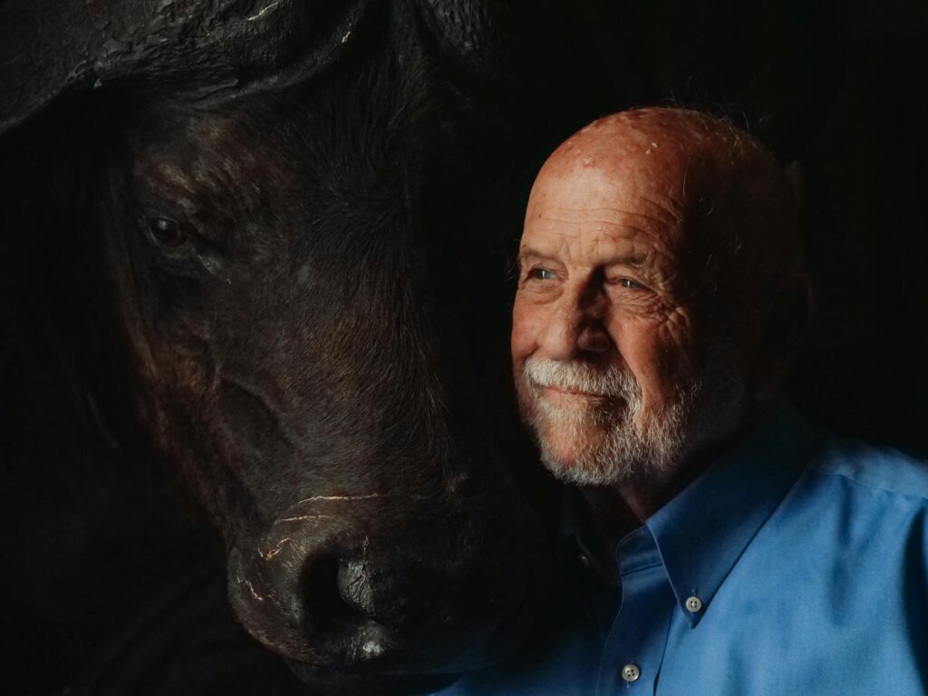 Portrait of an elderly man sharing a moment with a bison in dim lighting.